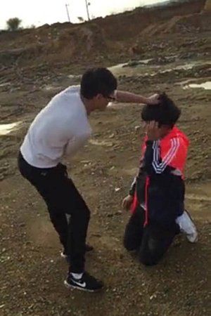 受害男生跪在沙地上,被一白衣男生揪住头发。视频截图