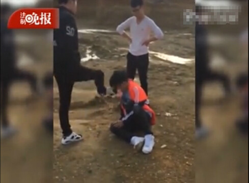 网传视频中,一名身穿红黑色外套的男生跪在地上,一名穿白色上衣的男生和一名穿黑色外套的男生对其轮番掌掴、踢打。(图片来源于网络)