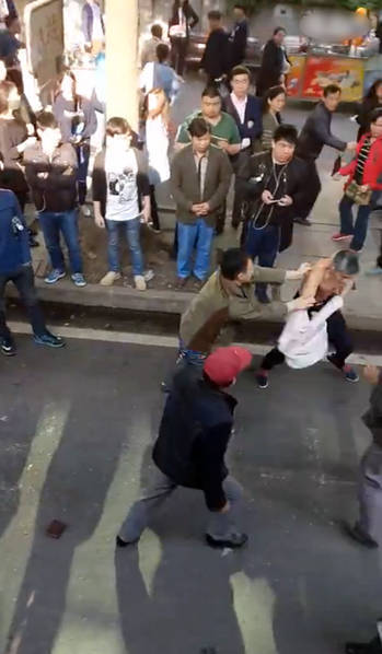 图为现场,男子和老人对打,捉住了老人的脖子,旁边很多路人围观。