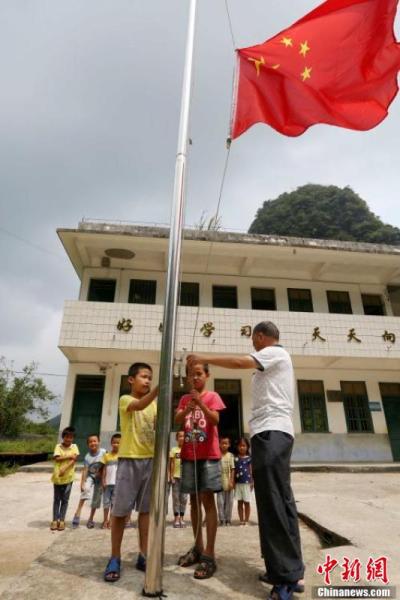 9月9日,在广西柳州市融安县东起乡长丰小学,李朝文教学生们升国旗。谭凯兴 摄