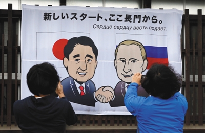 12月14日,日本长门市,民众在印有日本首相安倍晋三和俄罗斯总统普京卡通肖像的横幅前拍照。安倍晋三将于15日与来访的普京会谈。 图/视觉中国