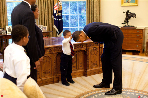 2009年5月8日，美国华盛顿，白宫工作人员家属参观白宫时，美国总统奥巴马在椭圆形办公室内俯下身来让一名小男孩摸自己的头发。