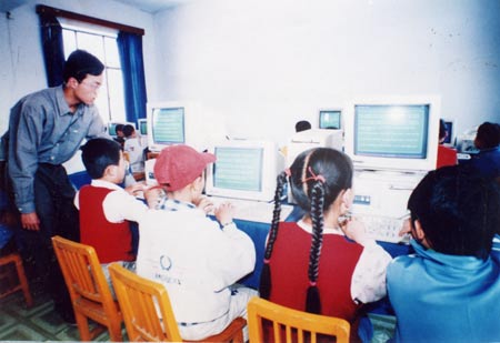 孩子们在大学生志愿者的指导下学习计算机的使用