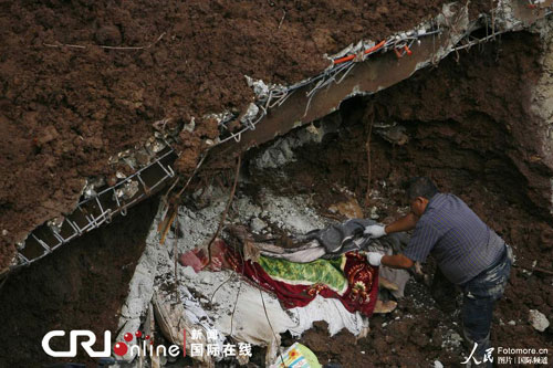 一名工人在山体滑坡压垮的房屋废墟下发现两名遇难者遗体