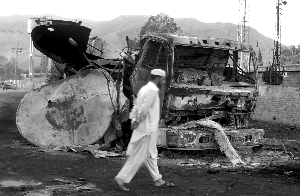 21日，巴基斯坦边境地区,袭击发生后，一名当地居民走过已经被烧毁的北约油罐车。