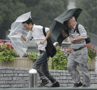 行人在狂风中勉强撑伞前行。