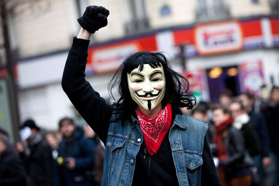图为一名戴面具的抗议者面对镜头挥舞拳头