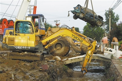 昨日，房山区青龙湖镇北车营村，救援队伍清理淤泥，一辆被洪水冲走受损的汽车被吊起。