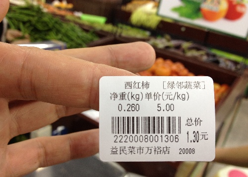 成都益民菜市场万裕店工作人员展示西红柿的价格标签,上面标注了蔬菜