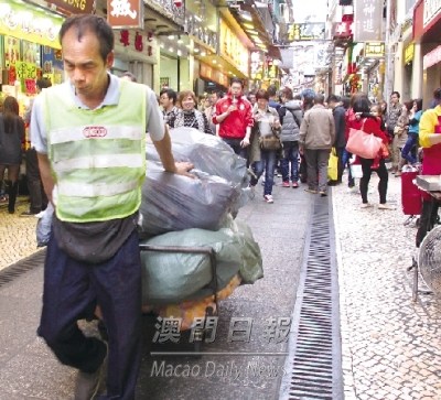 手信街狭窄，途人众多，清洁工人用手推车运走垃圾。澳门《澳门日报》