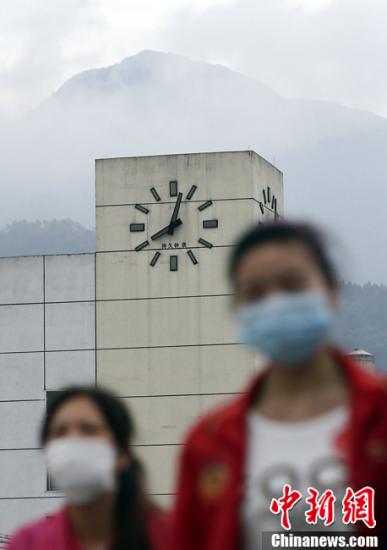 4月25日，两名戴着口罩的女子从四川芦山车站的时钟前走过，时钟一直停在发生地震的8点02分，目前震区防疫工作全面启动，成为这一阶段震区工作重点。中新社发 张浩 摄