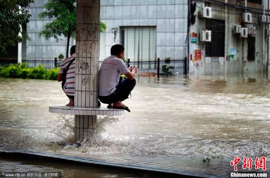 5月22日，广东省珠海市，两名市民被水困在公交车站台的“孤岛”上。当日，广东珠海迎来了强降雨，多处低洼地受浸严重，不少市民淌水过街。张洲 摄 CFP视觉中国