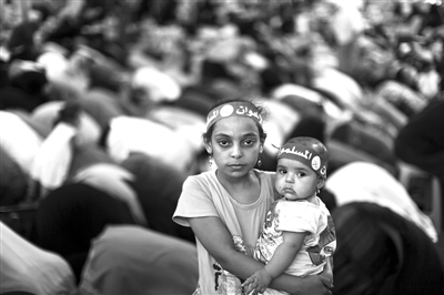 7月10日，埃及开罗一座清真寺外，一名女孩抱着一个幼儿。在其身后，穆斯林兄弟会和前总统穆尔西的支持者在祷告。