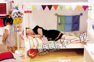 一位婆婆躺在儿童床上,想睡但又怕影响其他顾客购物。