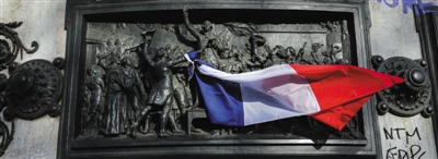 15日,在法国巴黎的共和国广场,人们将法国国旗挂在纪念碑上,悼念恐怖袭击遇难者。新华社记者 周磊 摄