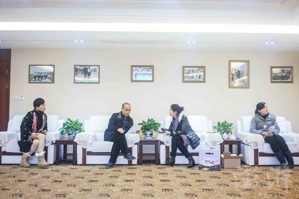 叶照辉在会议室和客户谈业务,墙上挂着各级政府领导来到公司考察的照片。