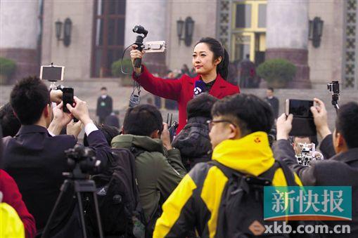 人民大会堂前,一位女记者持自拍稳定器直播,独自进行拍摄采访。