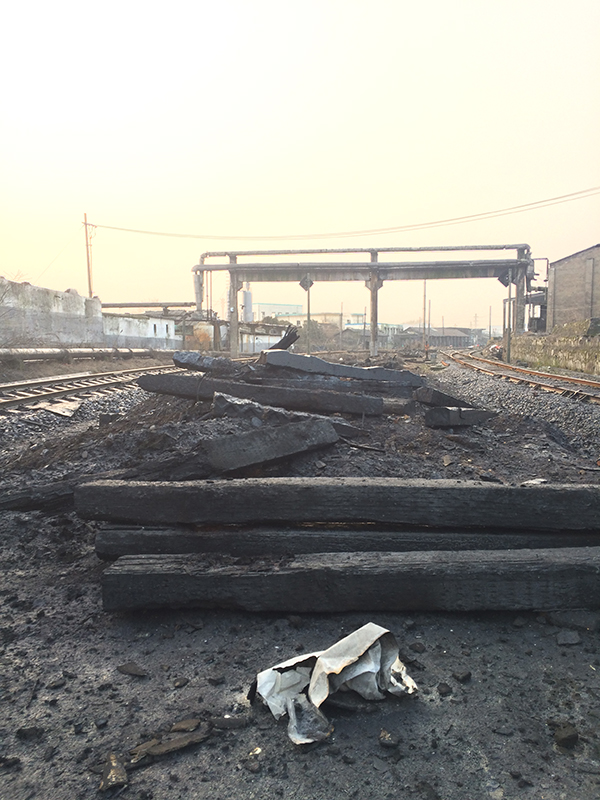 两条铁轨间堆了黑色木块、水泥块等,图中右侧为爆炸点,左边是另一工厂。